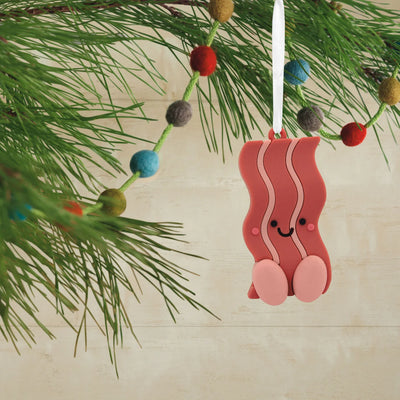 Christmas ornament set featuring two rubber ornaments: a smiling bacon slice and a smiling fried egg. They are connected by a red ribbon.