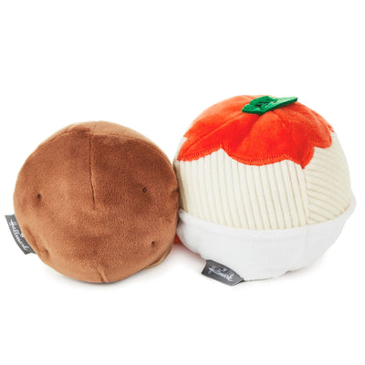 Two plush toys shaped like food sitting side-by-side.plush on the left is a red tomato with a green stem and leafy top.