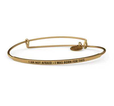 Gold bangle bracelet with the words "I am not afraid - I was born for this" engraved on it. The lettering is cursive.