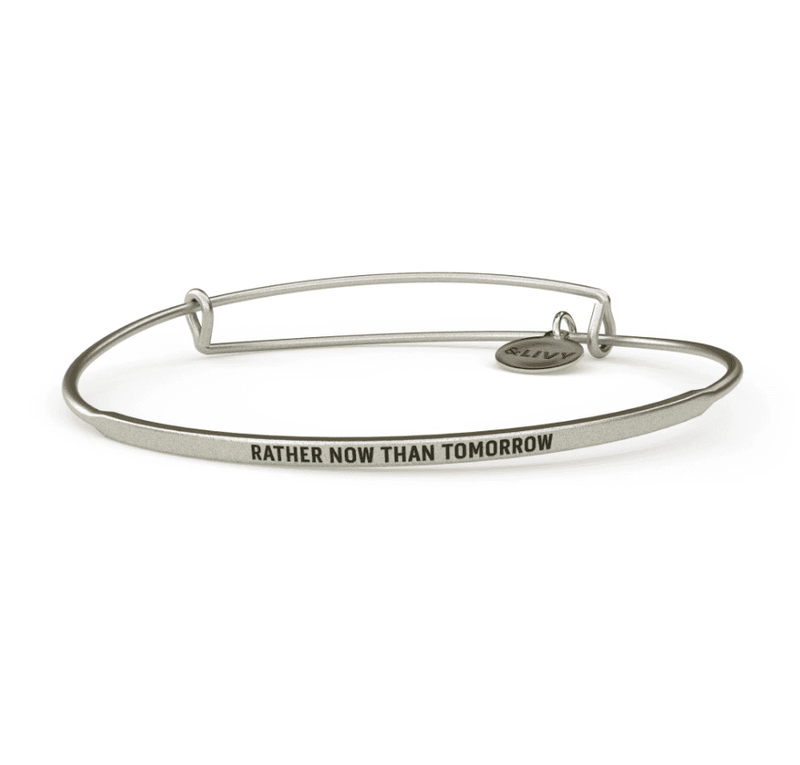 Silver bangle bracelet with the words "Rather Now Than Tomorrow" engraved on it. 