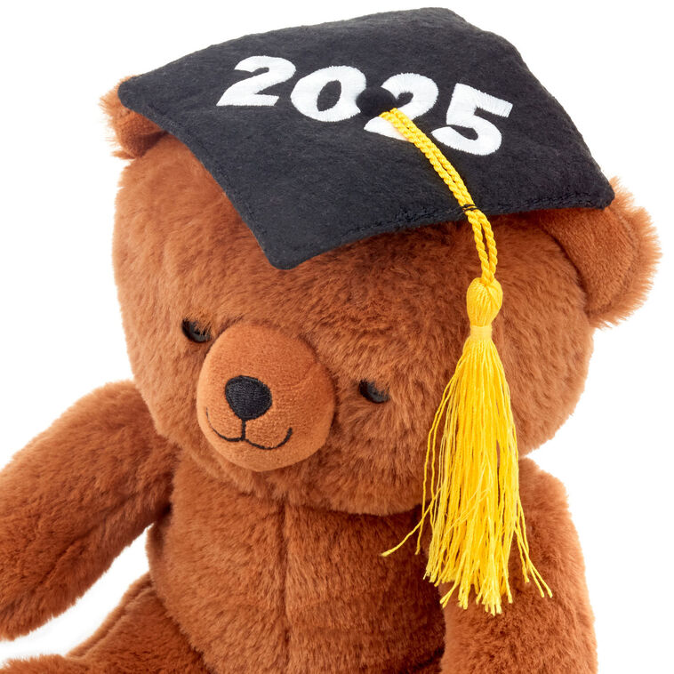 Brown plush teddy bear wearing a black graduation cap with a yellow tassel and embroidered &