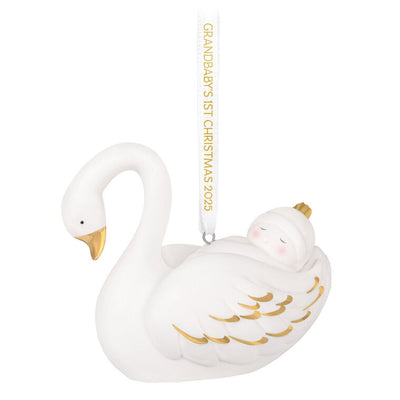 Porcelain Christmas ornament of a baby nestled in a swan’s wings, with gold accents and a commemorative 2025 ribbon

