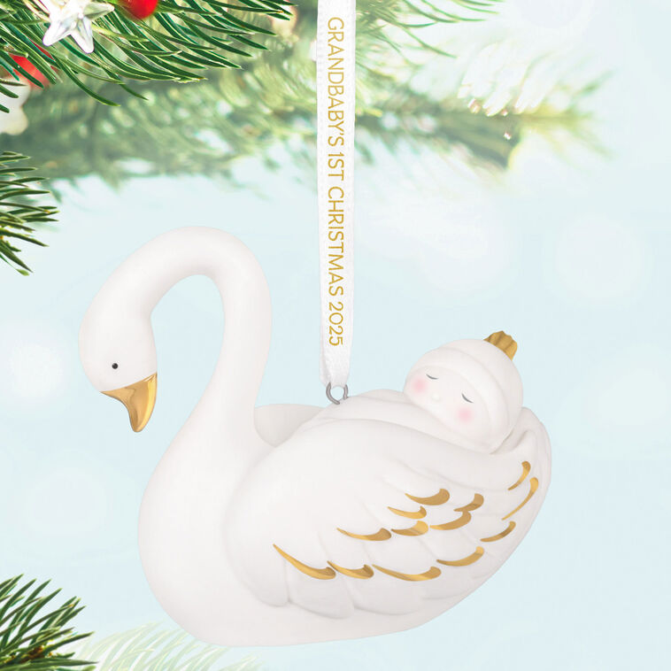 Porcelain Christmas ornament of a baby nestled in a swan’s wings, with gold accents and a commemorative 2025 ribbon

