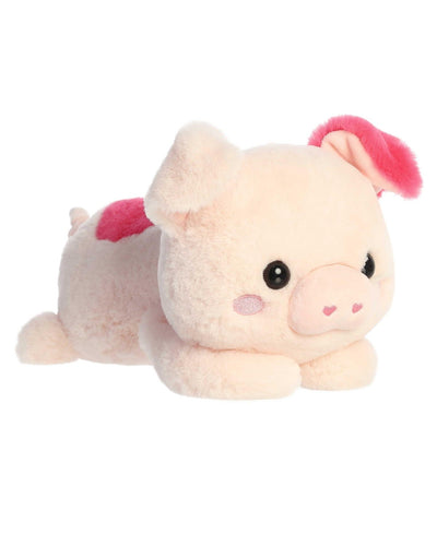 Penelope Pig plush by Aurora, in soft pink with red ear accents, lying belly-down in a cuddly Valentine’s Day pose.