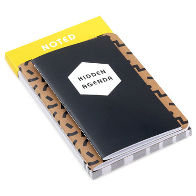 Stationery set with black and kraft notebooks and a memo pad featuring “Noted” and “Hidden Agenda” covers with geometric designs.
