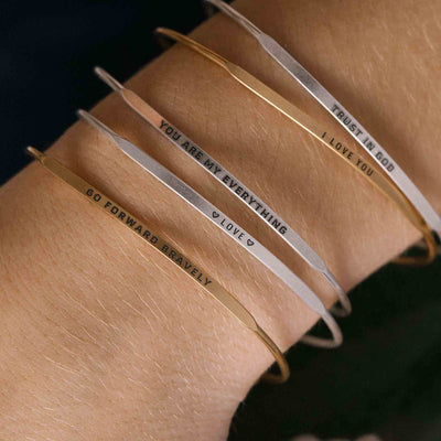 Stack of silver bangle bracelets with words engraved on them. Words include "TRUST IN GOD". 