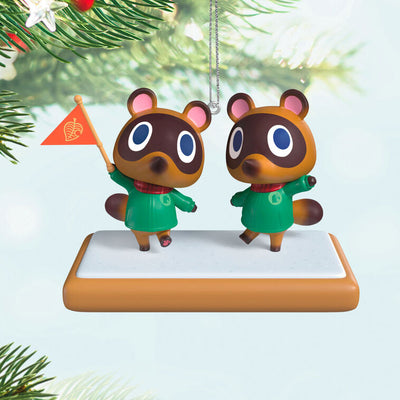 Hallmark Keepsake Nintendo Animal Crossing Timmy and Tommy ornament, twin raccoons with flag, green jackets, red scarves, on wood-style base.