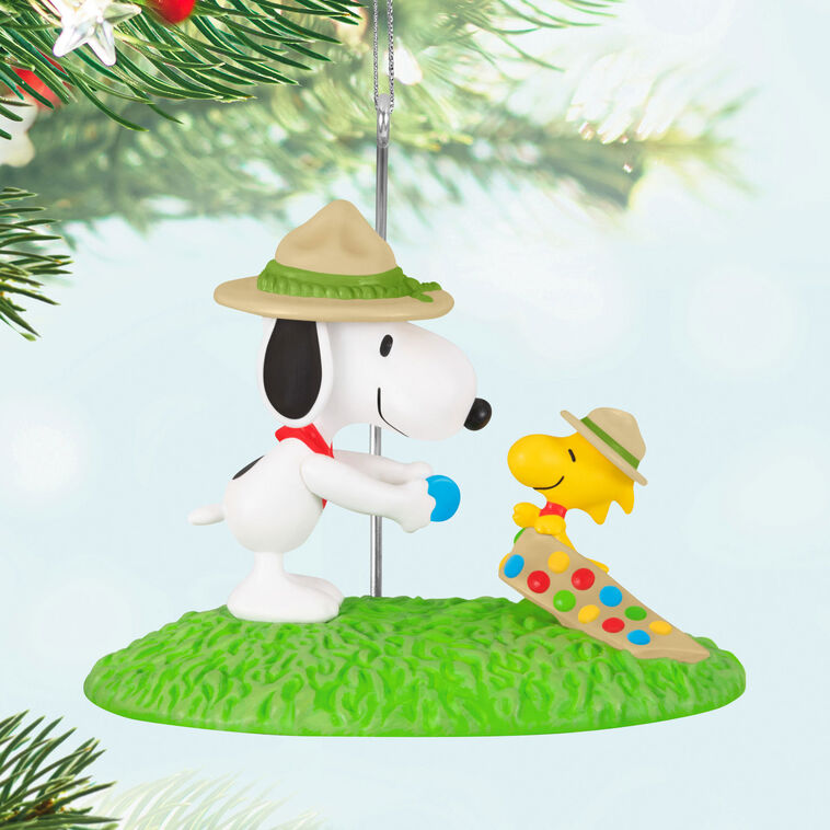 Snoopy in scout hat presenting merit badge to Woodstock in sash, standing on green grass, Hallmark Peanuts Christmas ornament collectible
