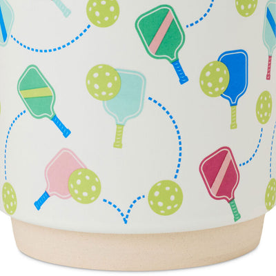 White ceramic pickleball mug with colorful paddle and ball icons, oversized handle, and stackable recessed base