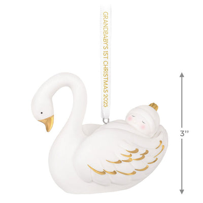 Porcelain Christmas ornament of a baby nestled in a swan’s wings, with gold accents and a commemorative 2025 ribbon

