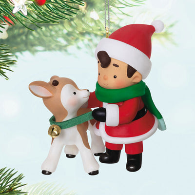 Hallmark Keepsake Young Santa ornament—Santa as a boy in red hat and coat, green scarf, placing green collar with gold bell on young reindeer
