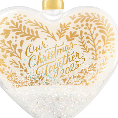 Glass heart Christmas ornament with snow, gold greenery accents, and “Our Christmas Together 2025” message.

