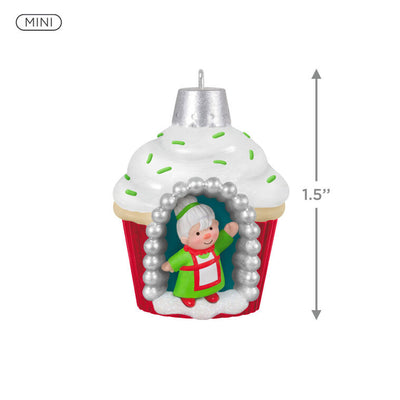 Mini cupcake-shaped ornament with Mrs. Claus waving from a silver-dotted doorway, topped with white icing and green sprinkles.