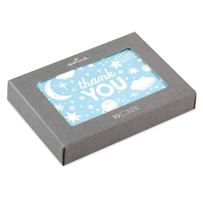 Blue thank-you cards with white embossed designs of a crescent moon, stars, clouds, and planets, shown with matching envelopes in a gift box.

