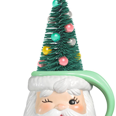 Green stocking hat mug ornament with winking Santa face and pastel ball-decorated bottlebrush tree inside

