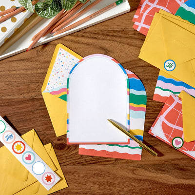 Stationery set with arched sheets in colorful wave and coral prints, yellow envelopes, and heart and star seal stickers.
