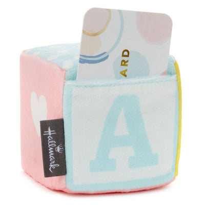 Pastel plush baby block with ABC design and pocket for holding a gift card or mini greeting card, featuring a rattle inside.

