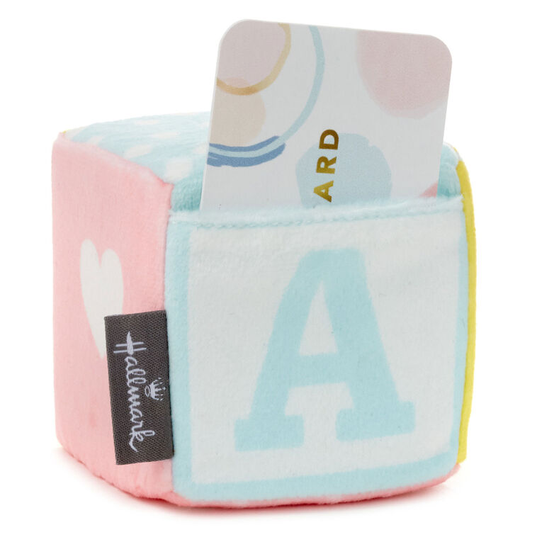 Pastel plush baby block with ABC design and pocket for holding a gift card or mini greeting card, featuring a rattle inside.

