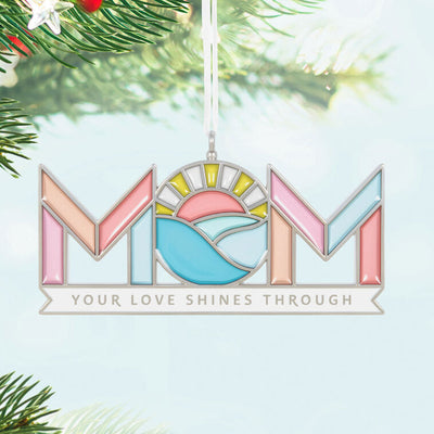 Stained-glass style metal ornament spelling “Mom” with sun and waves in the O, and banner reading “Your love shines through.”