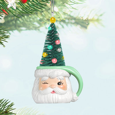 Green stocking hat mug ornament with winking Santa face and pastel ball-decorated bottlebrush tree inside

