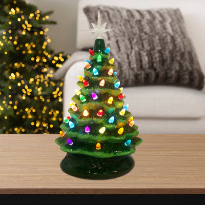 16-inch green ceramic Christmas tree with multicolored lights, placed on a table with a gray couch and holiday lights in the background