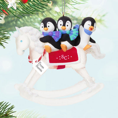Christmas ornament of playful penguins on a sparkling rocking horse with red and white monogrammed saddle