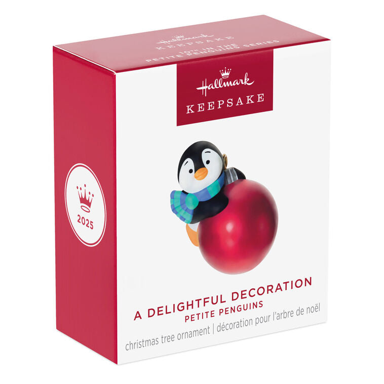 Mini penguin ornament holding a large red Christmas ball, wearing a blue plaid scarf with cheerful expression — Petite Penguins series.