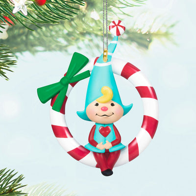 Hallmark Keepsake Sweet Peppermint girl gnome ornament in red and blue, sitting on candy cane wreath with green bow.
