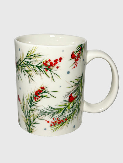 White ceramic mug with red holly berries and green pine branches in a festive botanical pattern.