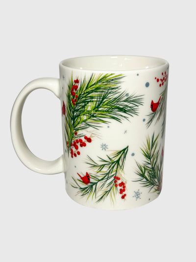 White ceramic mug with red holly berries and green pine branches in a festive botanical pattern.