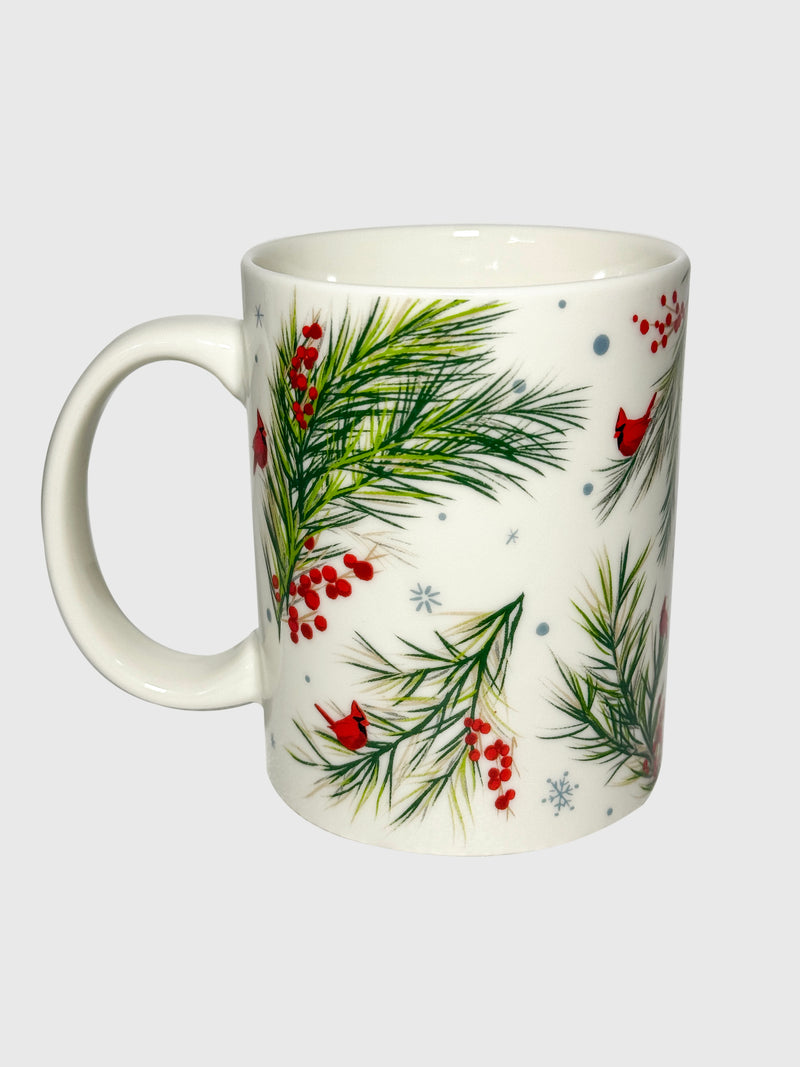 White ceramic mug with red holly berries and green pine branches in a festive botanical pattern.