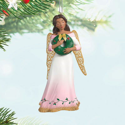 Hallmark Keepsake ornament of angel in pink and white gown with holly vines, holding a green wreath, gold metal wings, glitter accents