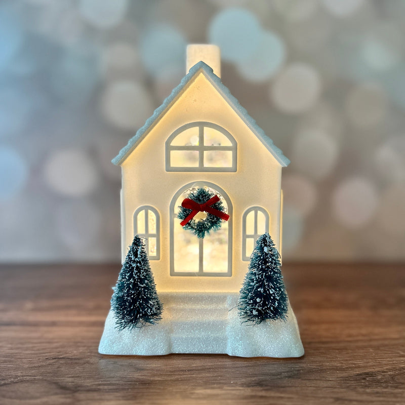 Assorted ivory and pink glittery Christmas houses with bottlebrush trees, wreaths, and warm light.
