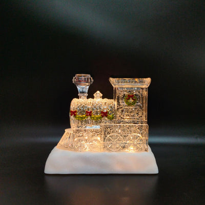 Glittering LED Christmas train with wreath accents, snowy base, and warm interior glow.
