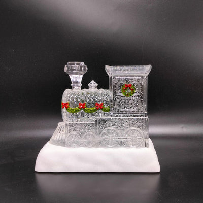 Glittering LED Christmas train with wreath accents, snowy base, and warm interior glow.
