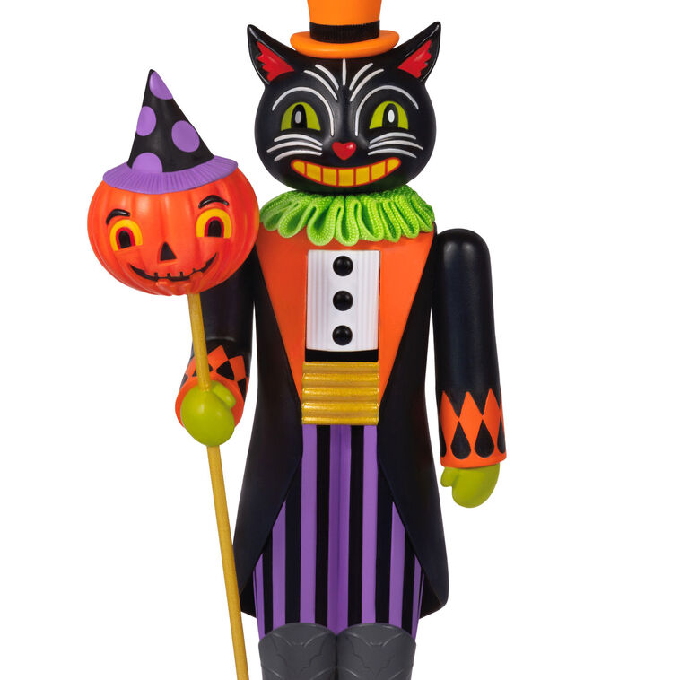 Black cat nutcracker ornament dressed as nobleman with top hat, colorful coat, and pumpkin staff on harlequin base