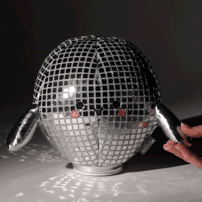 Smiling plush disco ball with silver sequins and arms, spins and plays 'Celebration' by Kool & the Gang.


