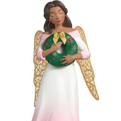 Hallmark Keepsake ornament of angel in pink and white gown with holly vines, holding a green wreath, gold metal wings, glitter accents
