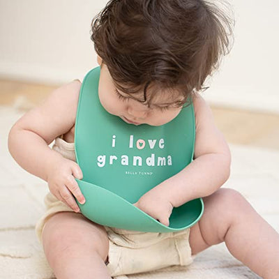 Pink silicone baby bib with “Love Grandma” phrase, features deep food-catching pocket and adjustable neck.

