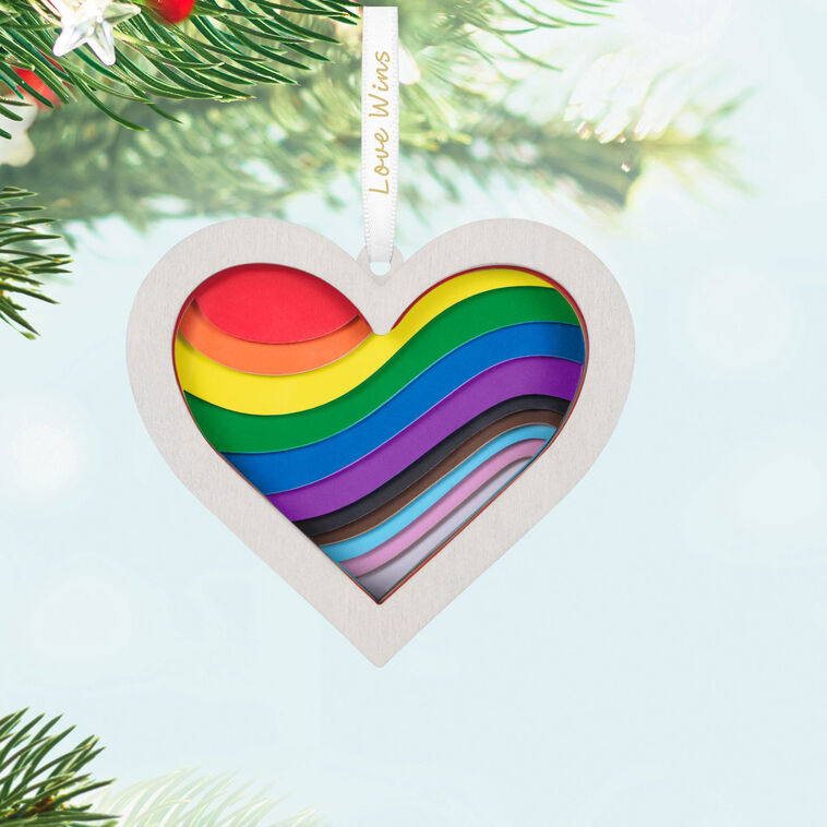 Heart-shaped rainbow papercraft ornament in a whitewashed wood frame with “Love Wins” ribbon for LGBTQIA holiday celebration.