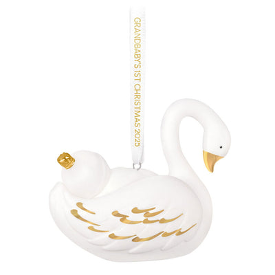 Porcelain Christmas ornament of a baby nestled in a swan’s wings, with gold accents and a commemorative 2025 ribbon

