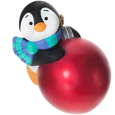 Mini penguin ornament holding a large red Christmas ball, wearing a blue plaid scarf with cheerful expression — Petite Penguins series.