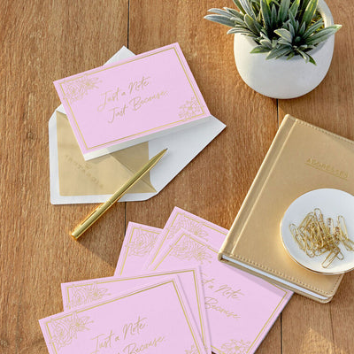 Rose pink blank note cards with gold script lettering and floral corner sketches in kraft box.
