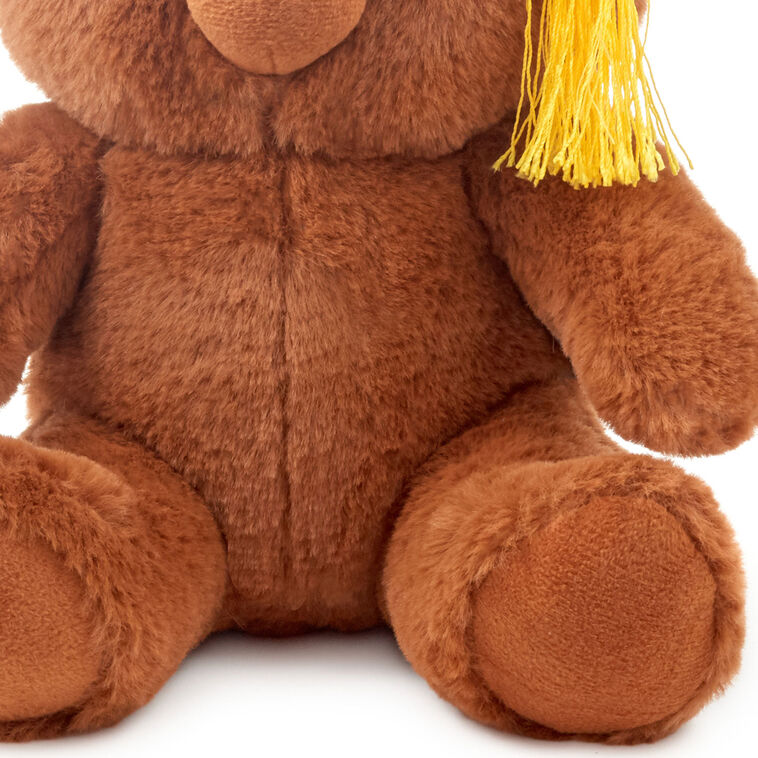 Brown plush teddy bear wearing a black graduation cap with a yellow tassel and embroidered &