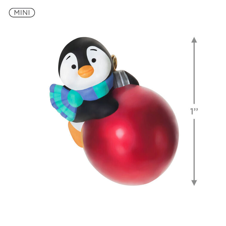 Mini penguin ornament holding a large red Christmas ball, wearing a blue plaid scarf with cheerful expression — Petite Penguins series.