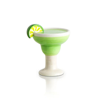 small, lime green margarita with a slice of lime on the rim sits in a clear glass with a white background. 