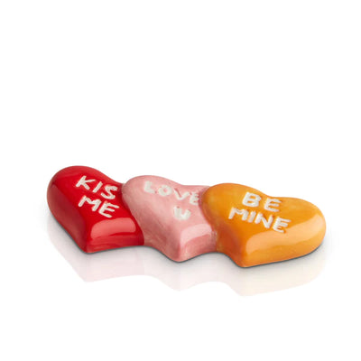 Row of conversation hearts in pastel colors stacked on a white background. Text on hearts includes "KISS", "LOVE", "BE MINE"