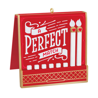 Red and gold matchbook-style ornament with “A Perfect Match” lettering and two heart-accented matchsticks