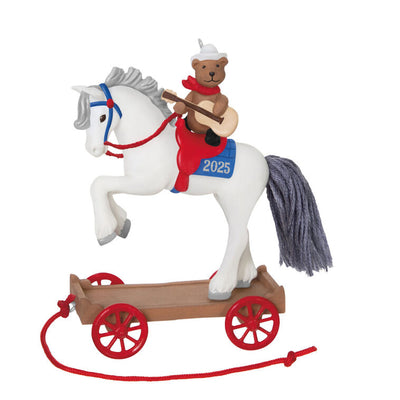 2025 ornament of a teddy bear cowboy on a white pony with red wheels, wearing a hat and scarf, strumming a guitar on a rolling wood-tone base.
