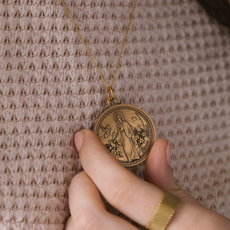 The pendant is gold and shaped like a rounded shield. The text "Divine Mother" is written around the edge of the pendant in a decorative font.